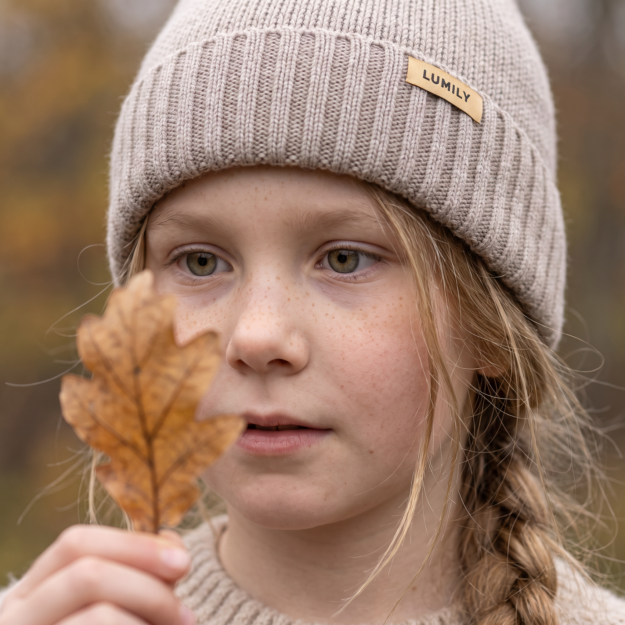 Barn iført Bark merinouldshue fra Lumily, udendørs med et efterårsblad i hånden